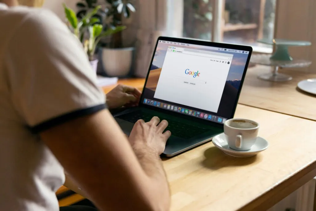 Man using Google search engine on a laptop with a cup of coffee